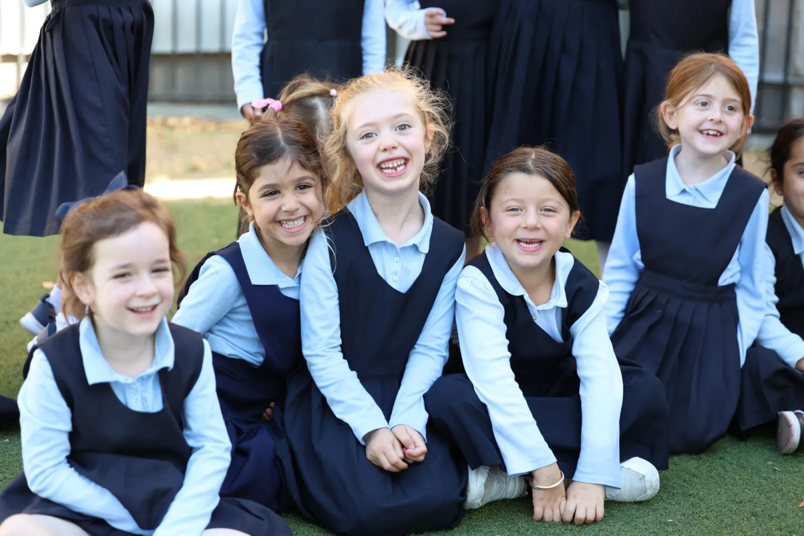 Young girls in uniform laughing together, sitting on the grass